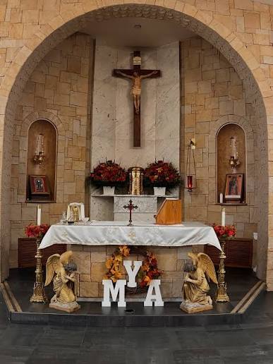 The sanctuary of Saint Maron Church: the altar beneath its stone arch, with a crucifix above and kneeling angels at either side.